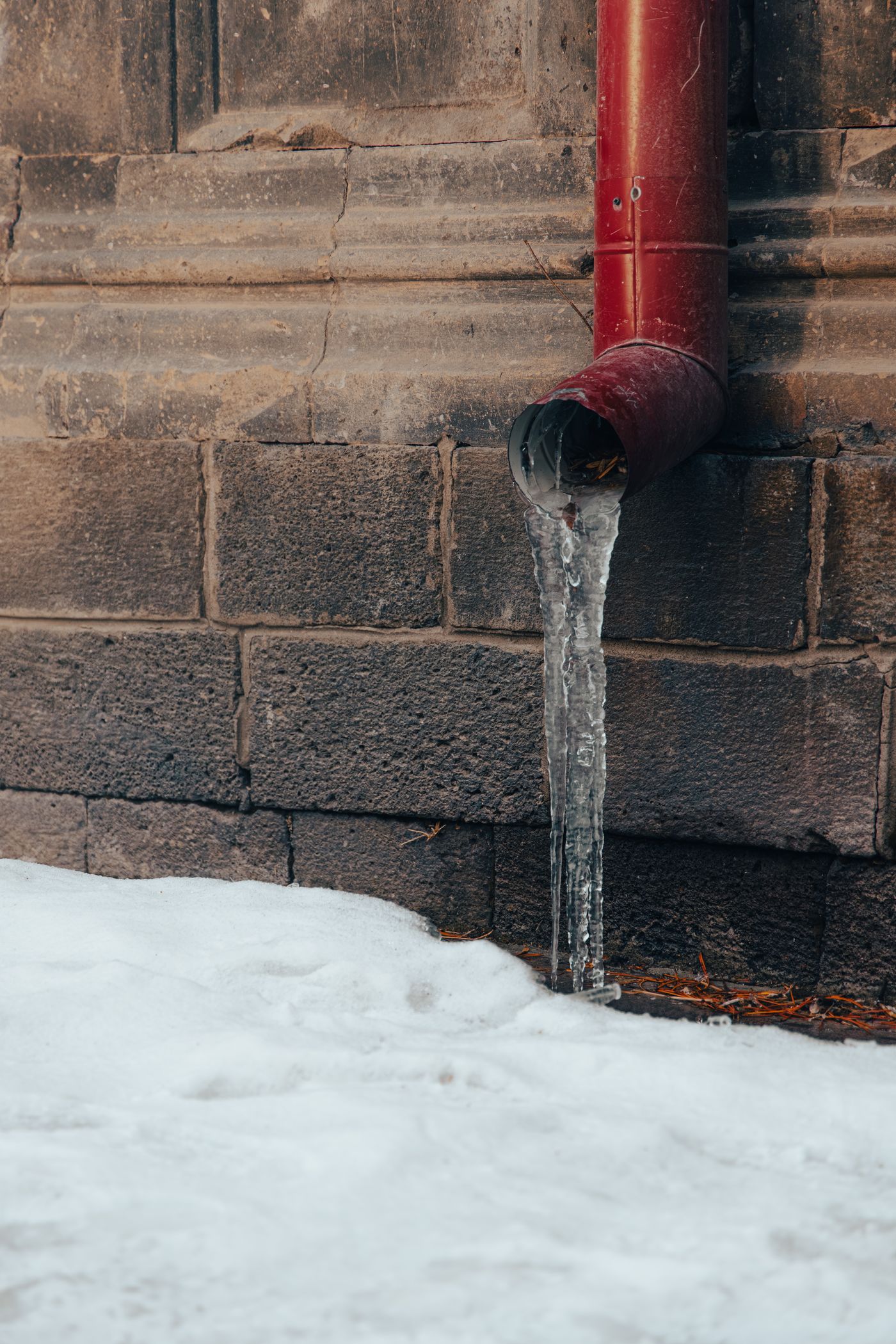 A frozen pipe dripping against a cold brick wall